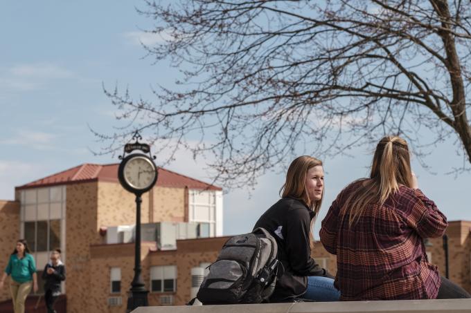 Two female students chat outside on an early spring day.