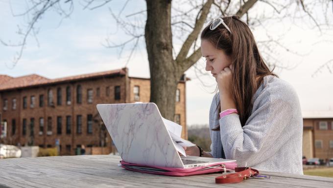 A female student works at her laptop near Francis Hall.