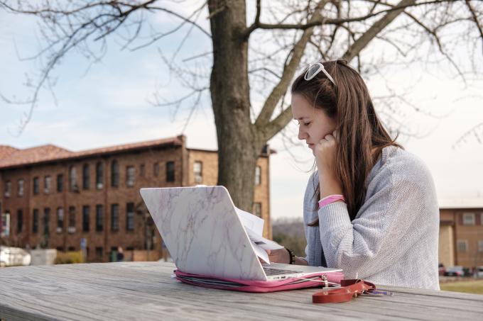 A female student works at her laptop near Francis Hall.