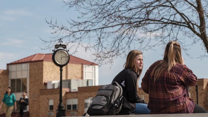 Two female students chat outside on an early spring day.